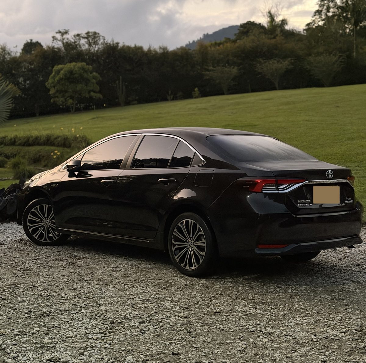 Toyota Corolla negro recién lavado al atardecer, frente a un prado y la montaña