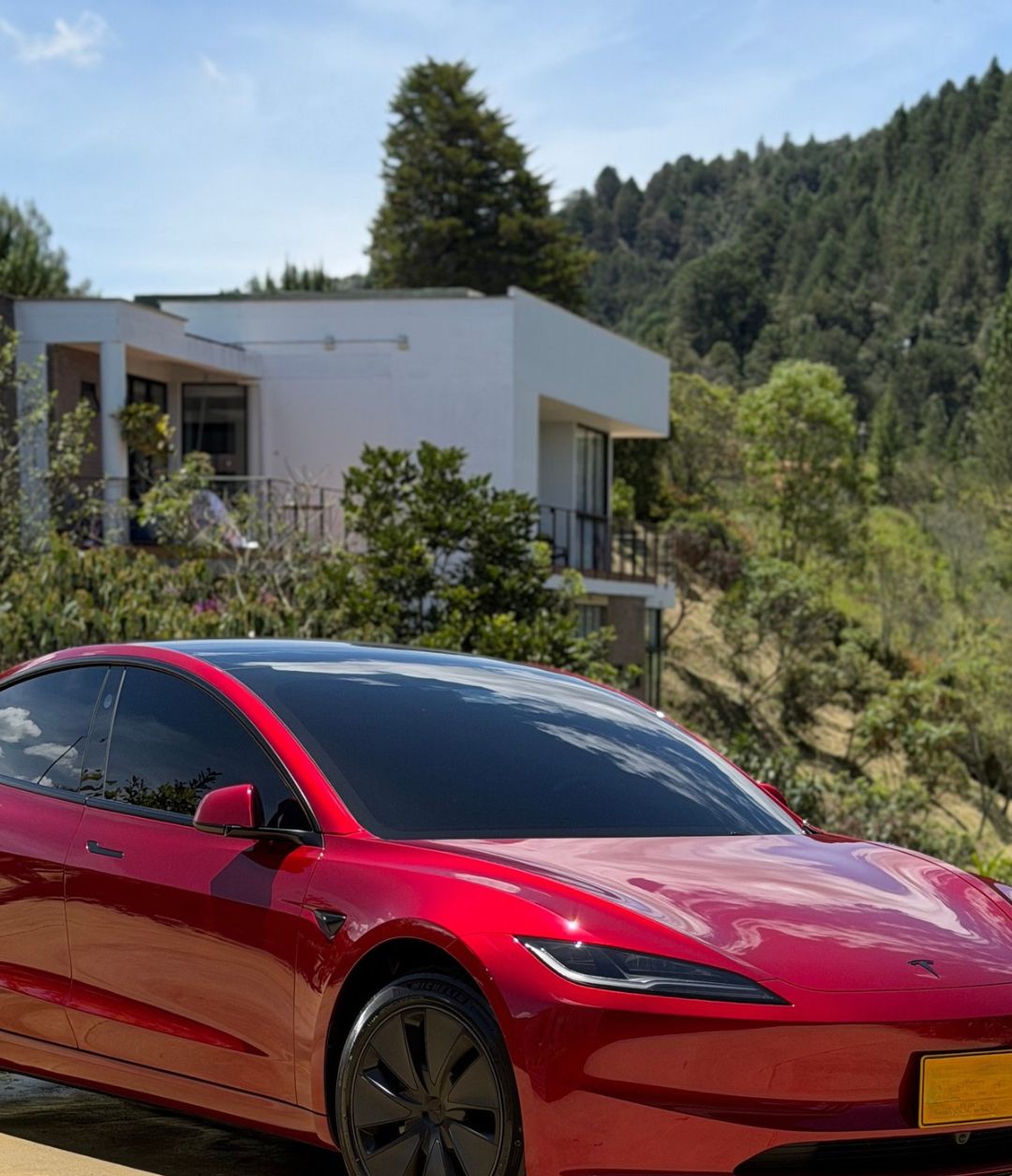 Tesla Model 3 rojo brillante frente a una casa en la montaña